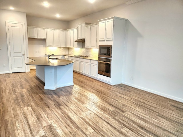 kitchen featuring hardwood / wood-style floors, stainless steel appliances, an island with sink, and white cabinetry