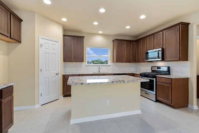 kitchen featuring light stone countertops, stainless steel appliances, sink, light tile patterned floors, and a center island