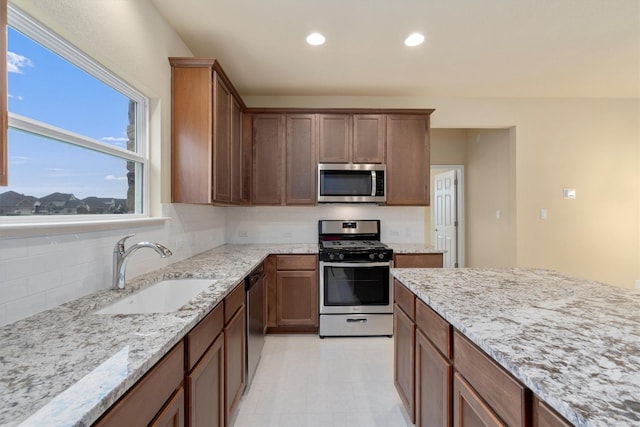 kitchen featuring backsplash, light stone counters, sink, and appliances with stainless steel finishes