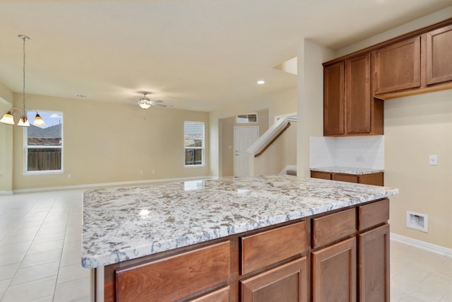 kitchen featuring light stone counters, a kitchen island, light tile patterned flooring, and ceiling fan with notable chandelier