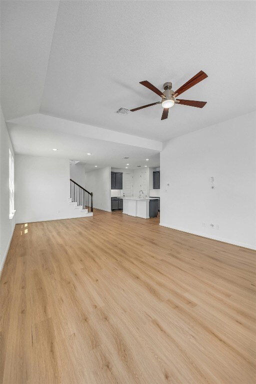 unfurnished living room featuring light wood-style flooring, visible vents, ceiling fan, and stairway