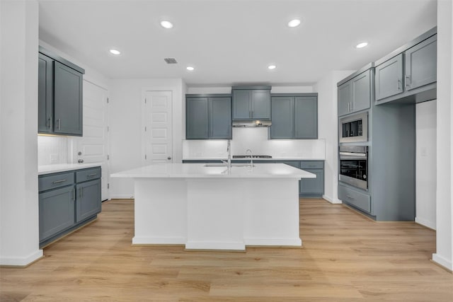 kitchen featuring oven, under cabinet range hood, visible vents, light countertops, and a center island with sink