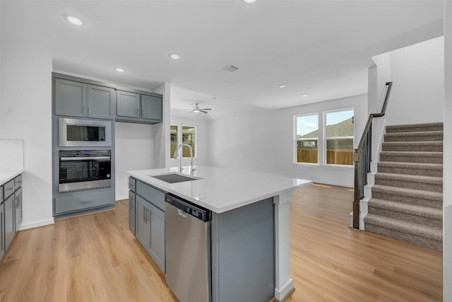 kitchen with light countertops, appliances with stainless steel finishes, a sink, and a center island with sink