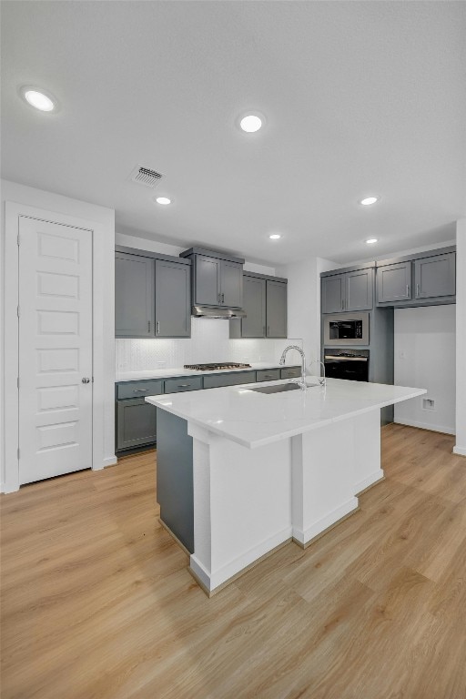 kitchen featuring gray cabinets, light countertops, and an island with sink