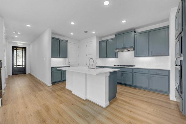 kitchen featuring appliances with stainless steel finishes, a kitchen island with sink, light countertops, under cabinet range hood, and a sink