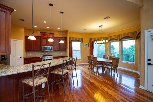 kitchen featuring pendant lighting, dark hardwood / wood-style flooring, backsplash, appliances with stainless steel finishes, and a breakfast bar area