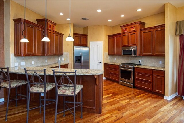 kitchen with decorative light fixtures, hardwood / wood-style floors, tasteful backsplash, and stainless steel appliances