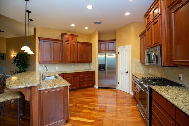 kitchen featuring light hardwood / wood-style floors, hanging light fixtures, stainless steel appliances, kitchen peninsula, and a kitchen breakfast bar