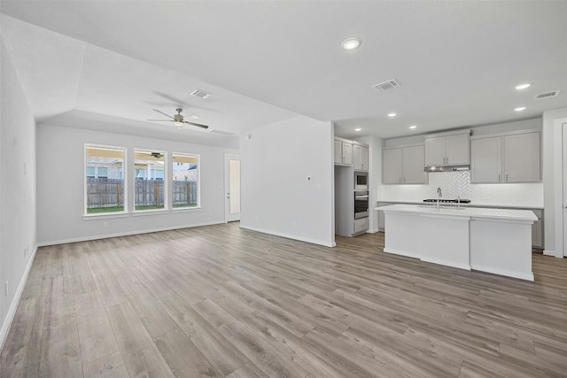 kitchen featuring ceiling fan, light hardwood / wood-style flooring, a center island with sink, and decorative backsplash