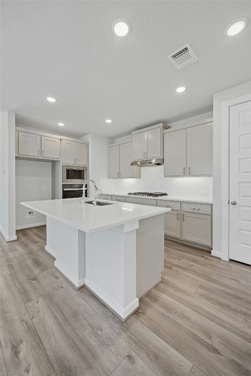 kitchen with white cabinets, light hardwood / wood-style floors, sink, a center island with sink, and stainless steel appliances