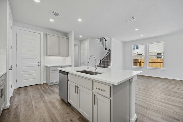 kitchen featuring light hardwood / wood-style floors, decorative backsplash, stainless steel dishwasher, sink, and a center island with sink