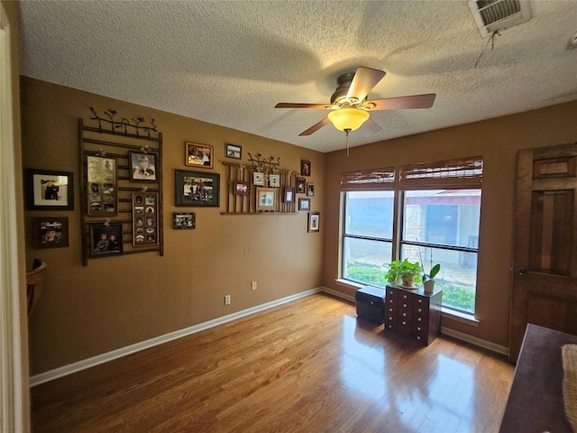 living area featuring hardwood / wood-style flooring, ceiling fan, and a textured ceiling