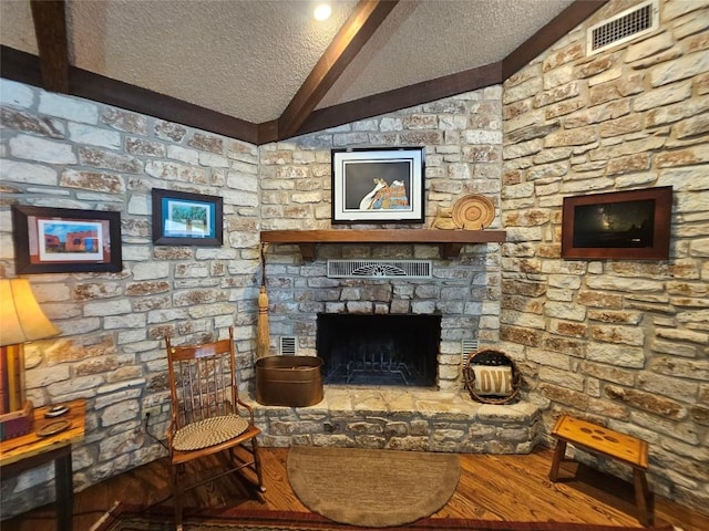 living room featuring a textured ceiling, hardwood / wood-style flooring, a stone fireplace, and lofted ceiling