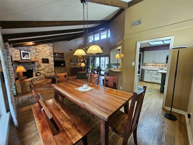 dining space with beam ceiling, high vaulted ceiling, a notable chandelier, dark hardwood / wood-style floors, and a stone fireplace