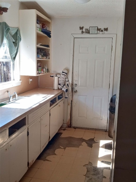 kitchen with sink, white cabinetry, a textured ceiling, and light tile floors