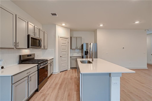 kitchen with tasteful backsplash, appliances with stainless steel finishes, sink, light wood-type flooring, and an island with sink