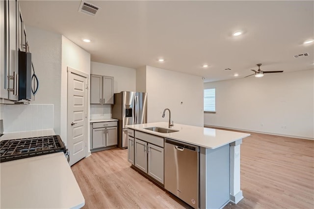 kitchen with an island with sink, light hardwood / wood-style flooring, sink, gray cabinets, and appliances with stainless steel finishes