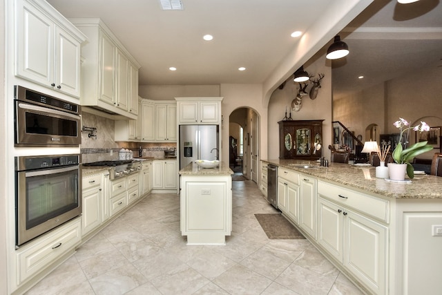 kitchen featuring appliances with stainless steel finishes, a center island, light tile floors, and light stone counters