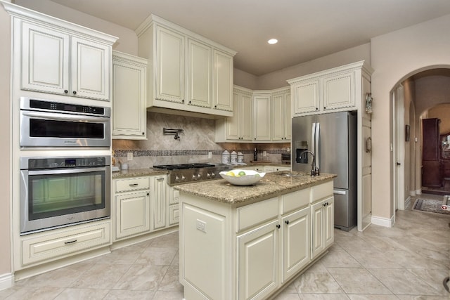 kitchen featuring a kitchen island, stainless steel appliances, tasteful backsplash, light stone counters, and light tile floors