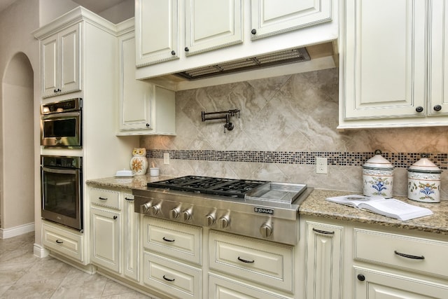 kitchen featuring backsplash, stainless steel appliances, light tile flooring, and light stone counters