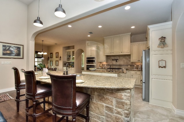 kitchen featuring cream cabinets, backsplash, stainless steel appliances, sink, and pendant lighting