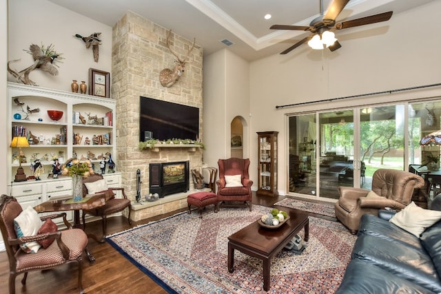 living room featuring a stone fireplace, a towering ceiling, ceiling fan, and hardwood / wood-style floors