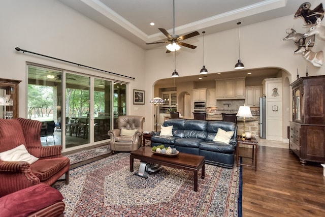 living room with ceiling fan, hardwood / wood-style flooring, a tray ceiling, and a towering ceiling