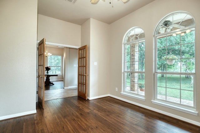 spare room featuring a healthy amount of sunlight, ceiling fan with notable chandelier, and dark hardwood / wood-style flooring