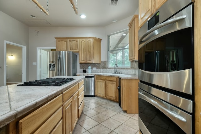 kitchen with tile counters, stainless steel appliances, tasteful backsplash, rail lighting, and sink