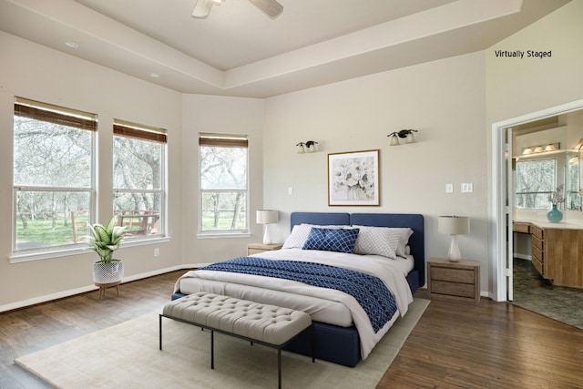 bedroom featuring connected bathroom, ceiling fan, dark hardwood / wood-style floors, and a tray ceiling