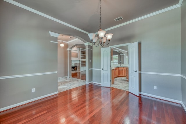 empty room with wood-type flooring, a chandelier, sink, and crown molding