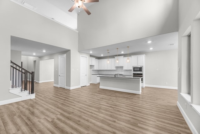 unfurnished living room featuring ceiling fan, light hardwood / wood-style flooring, a towering ceiling, and sink