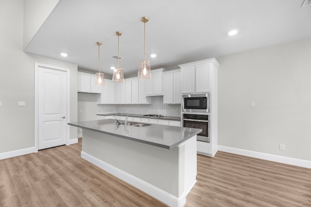 kitchen featuring light hardwood / wood-style floors, white cabinetry, appliances with stainless steel finishes, an island with sink, and backsplash