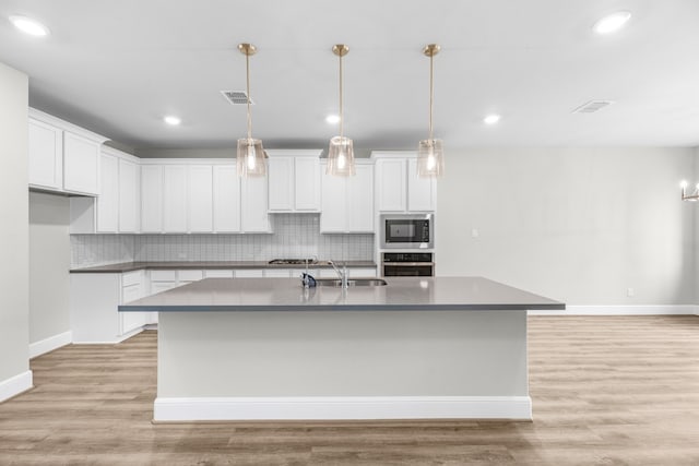 kitchen with stainless steel appliances, light hardwood / wood-style floors, a center island with sink, and backsplash