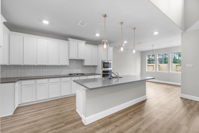 kitchen featuring light hardwood / wood-style floors, appliances with stainless steel finishes, white cabinets, backsplash, and pendant lighting