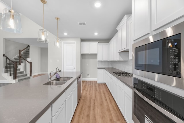 kitchen featuring stainless steel appliances, light wood-type flooring, pendant lighting, backsplash, and white cabinets