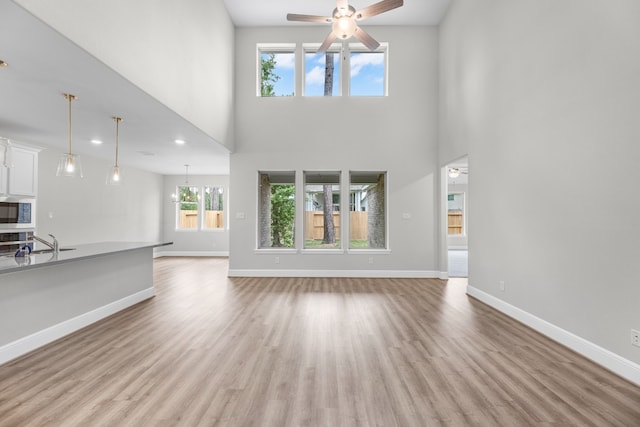 unfurnished living room with a towering ceiling, sink, ceiling fan, and hardwood / wood-style floors