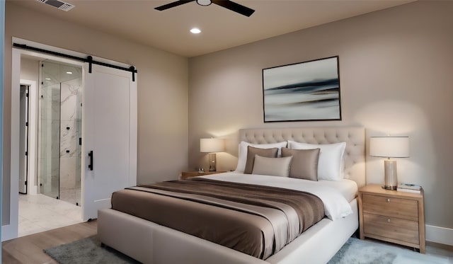 bedroom featuring a barn door, light hardwood / wood-style floors, and ceiling fan