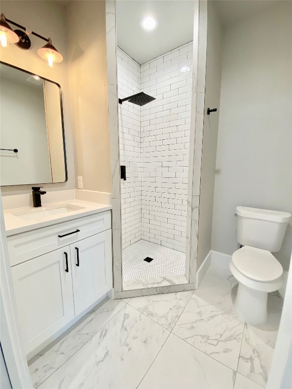 bathroom with tile flooring, vanity with extensive cabinet space, toilet, and a tile shower