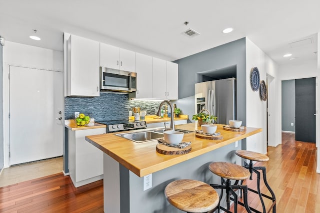 kitchen with white cabinets, a center island with sink, light wood-type flooring, and stainless steel appliances