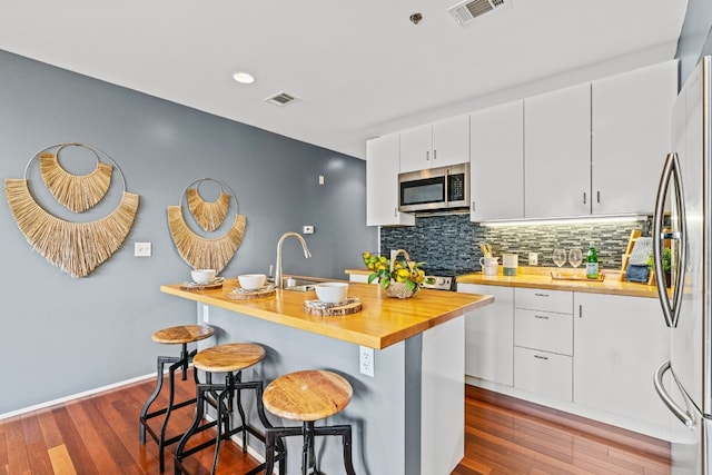 kitchen with appliances with stainless steel finishes, white cabinetry, tasteful backsplash, a breakfast bar area, and wood-type flooring