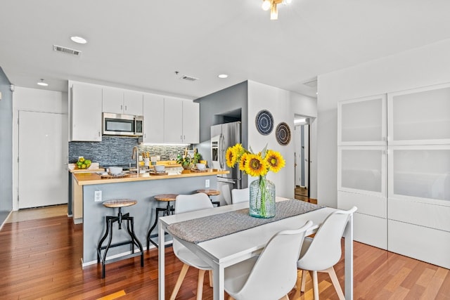 kitchen with wood-type flooring, white cabinetry, a kitchen breakfast bar, stainless steel appliances, and backsplash