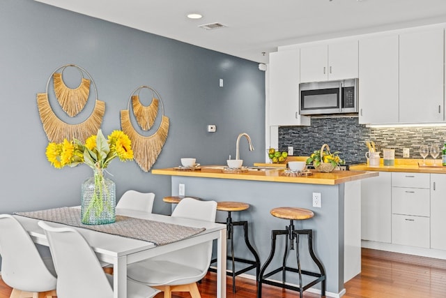 kitchen with light hardwood / wood-style floors, white cabinets, a breakfast bar, butcher block counters, and sink