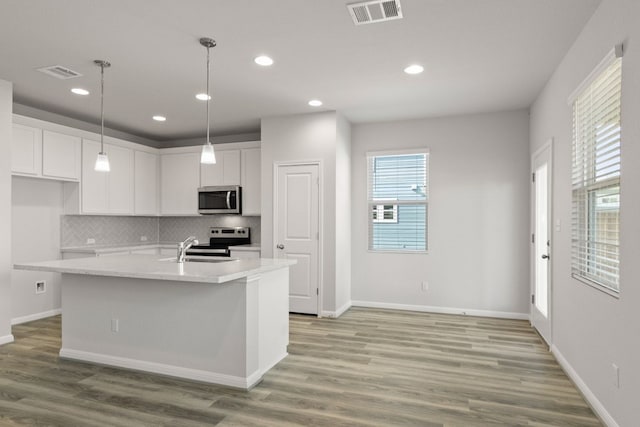 kitchen with stainless steel appliances, a center island with sink, light stone counters, white cabinets, and light hardwood / wood-style flooring