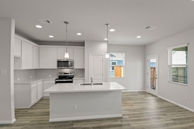 kitchen featuring stainless steel appliances, light hardwood / wood-style floors, white cabinets, and an island with sink