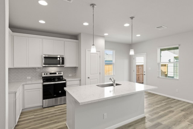 kitchen featuring stainless steel appliances, white cabinetry, sink, hanging light fixtures, and an island with sink