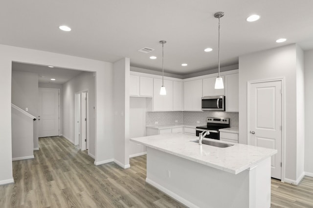 kitchen featuring a center island with sink, stainless steel appliances, light wood-type flooring, light stone countertops, and white cabinets