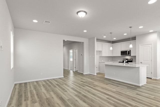 kitchen featuring stainless steel appliances, white cabinetry, a center island with sink, hanging light fixtures, and light hardwood / wood-style flooring