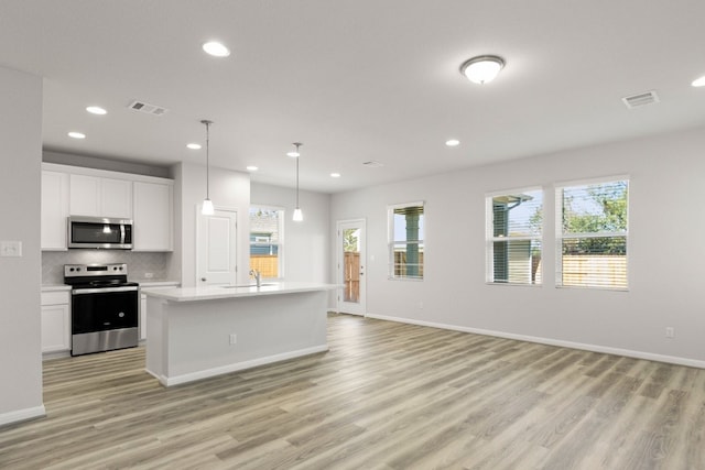 kitchen with white cabinetry, appliances with stainless steel finishes, an island with sink, light hardwood / wood-style flooring, and pendant lighting