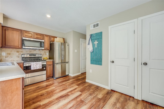 kitchen with tasteful backsplash, stainless steel appliances, sink, and light wood-type flooring